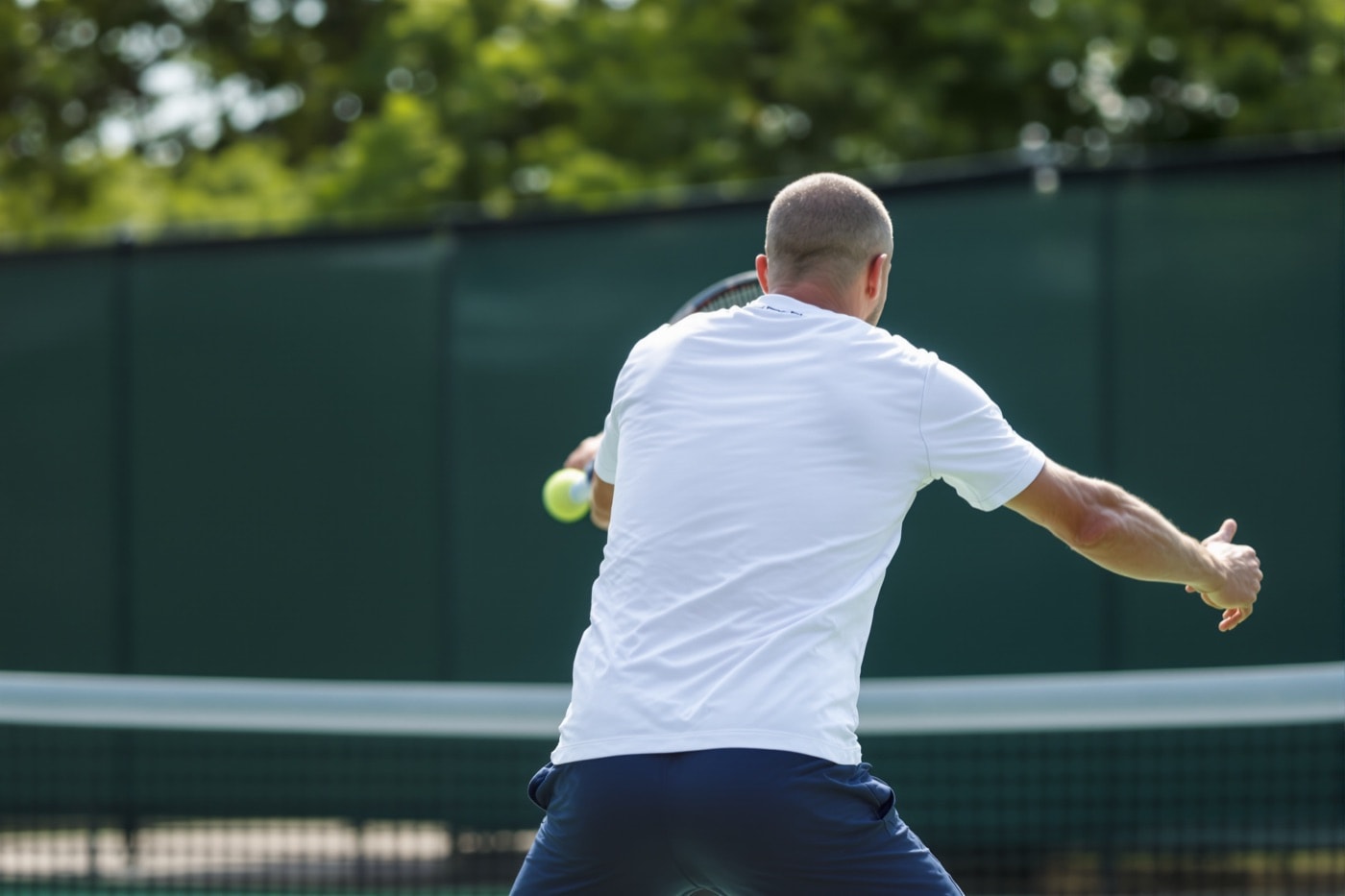 Tennis player seen from behind following through on a one-handed backhand, hitting arm extended and opposite arm swept back