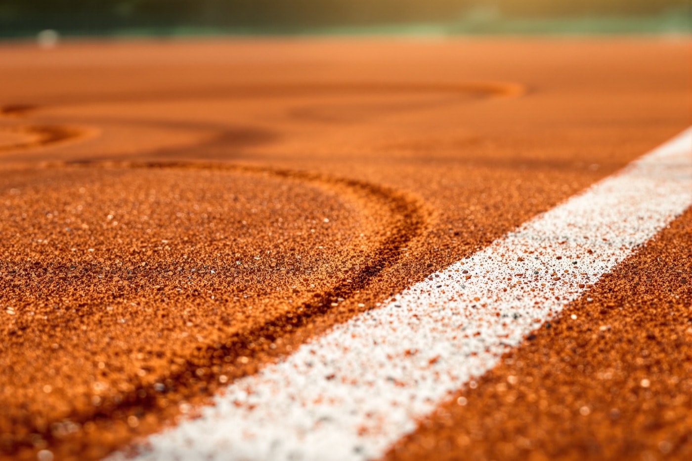 Close-up of a red clay court surface showing a white line and drag-broom patterns in the loose top layer